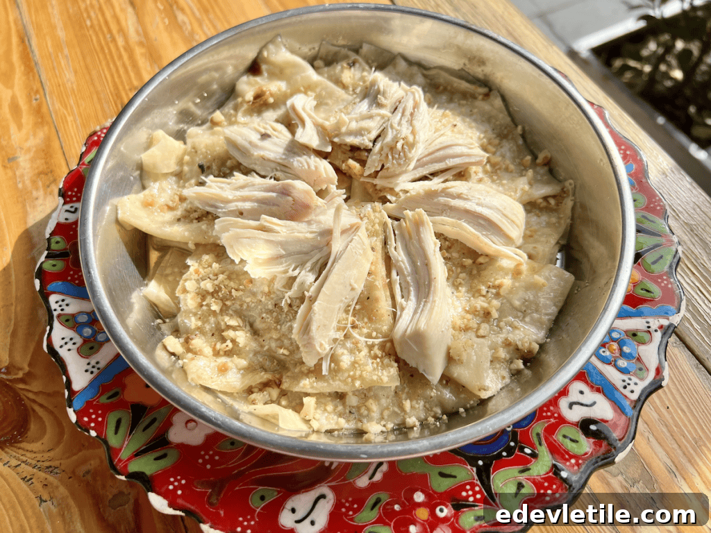 Traditional Kastamonu dish called Banduma, made of shredded chicken layered over flatbread and walnuts, served in a rustic metal bowl.