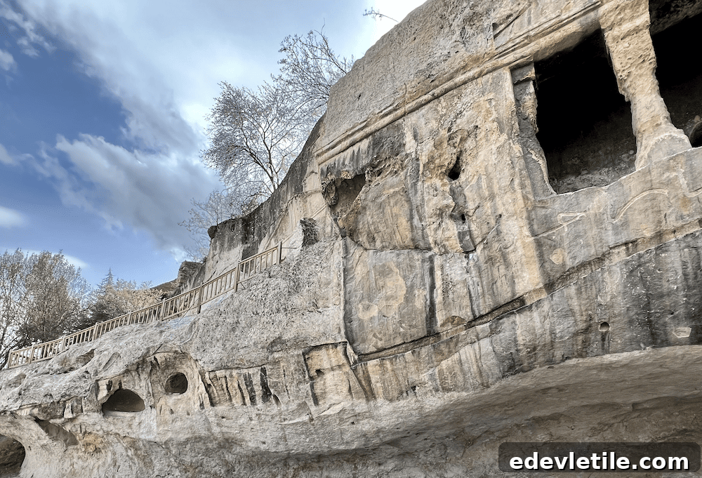 View of rock-cut tombs and ancient carvings in the stone cliffs of Kastamonu, with a wooden walkway along the edge.
