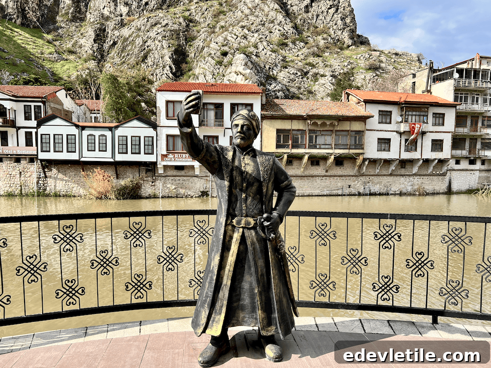Humorous bronze statue of an Ottoman man holding a smartphone for a selfie, set against Amasya’s river and traditional buildings.