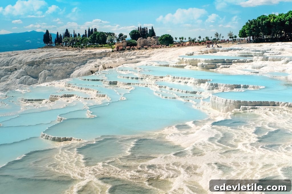 Bright blue mineral pools cascading down Pamukkale’s famous white travertine terraces, surrounded by greenery and distant hills.
