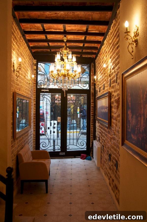Warmly lit entrance hallway with exposed brick walls, chandeliers, and wrought iron glass doors leading to the street outside.