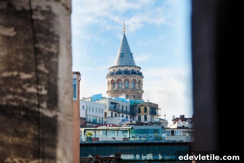 Distant view of the Galata Tower between two buildings, with a clear blue sky and surrounding residential rooftops in sight.