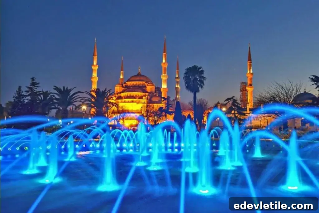 Night view of the Blue Mosque in Istanbul, dramatically lit in warm tones behind vibrant blue fountain lights in the foreground.