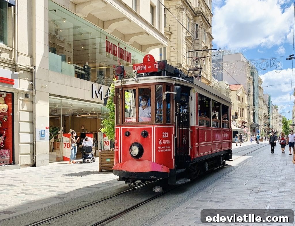 Historic red tram moving along Istiklal Avenue in Istanbul, surrounded by modern shops and pedestrians enjoying the bustling shopping street.