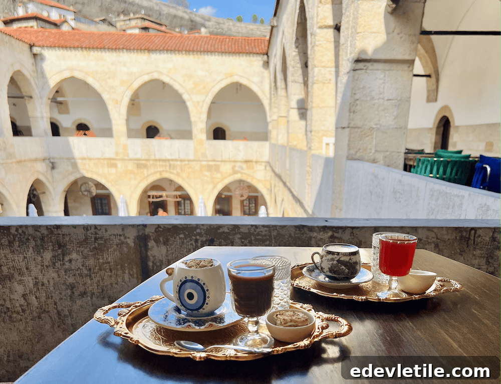 A table set with traditional Turkish coffee, water, and syrup drinks on gold trays, set in the upper gallery of a historic Safranbolu caravanserai courtyard.