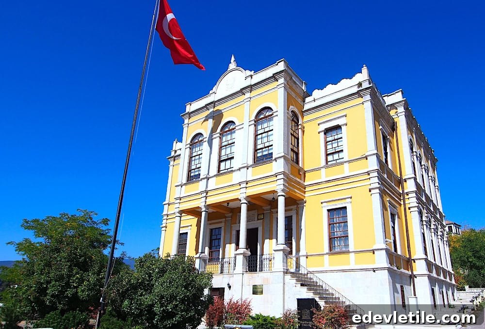 A grand historic yellow municipal building with arched windows and columns, set beneath a bright blue sky with a large Turkish flag waving.