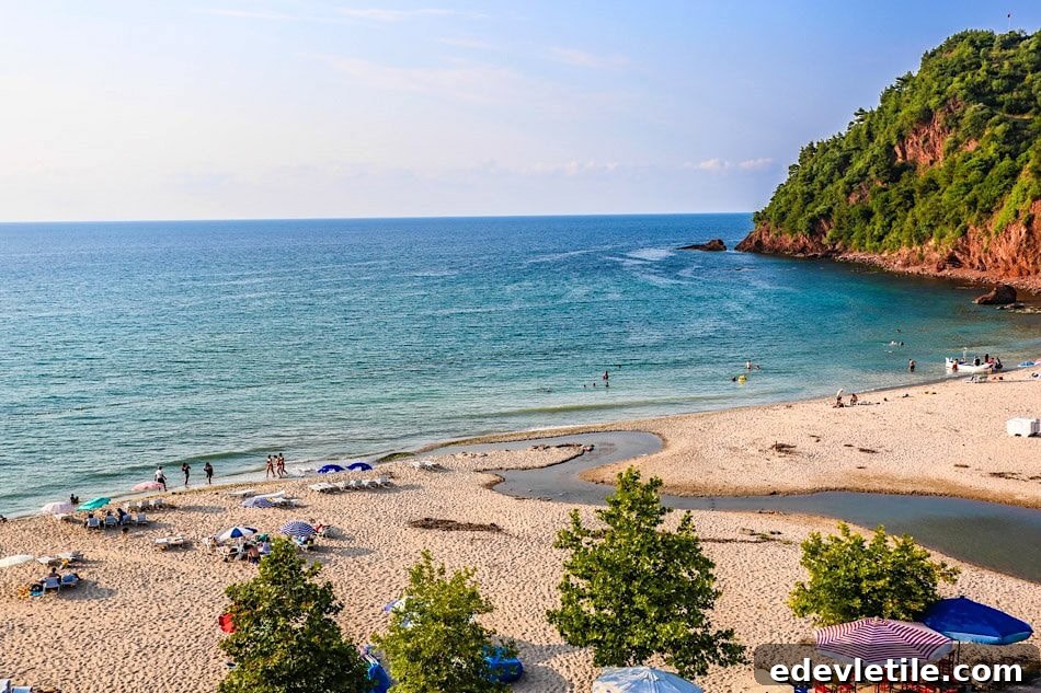 Golden sand and turquoise water at a beach near Amasra, with beachgoers, umbrellas, and a green hillside in the distance.