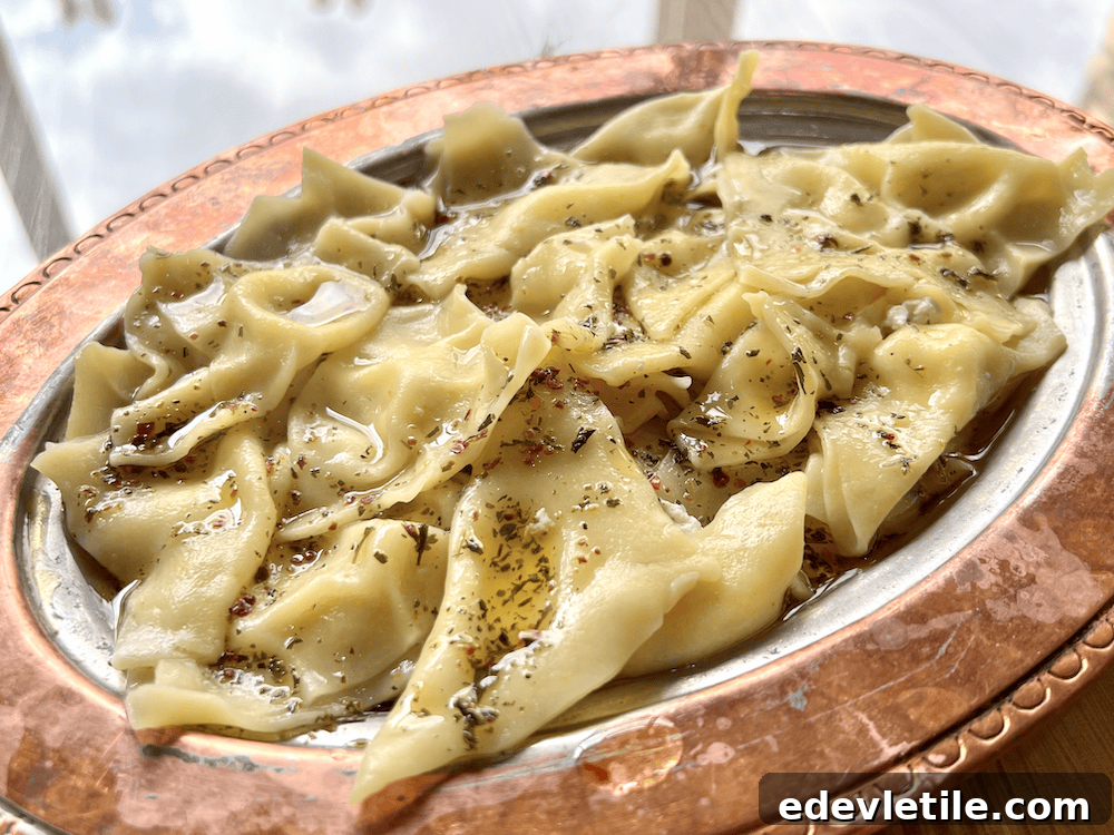 Close-up of a silver tray filled with handmade Safranbolu-style mantı (called peruhi), drizzled with butter and sprinkled with dried herbs.