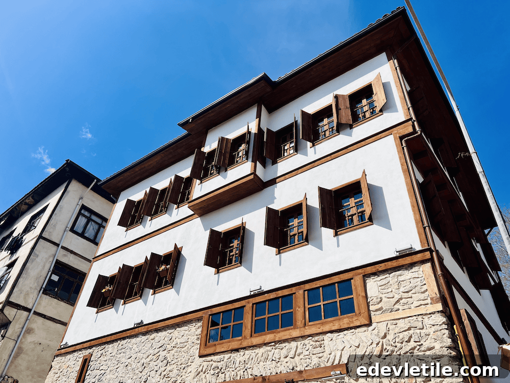 Whitewashed three-story Ottoman-style house with dark wood trim and shutters, photographed from below against a bright blue sky.
