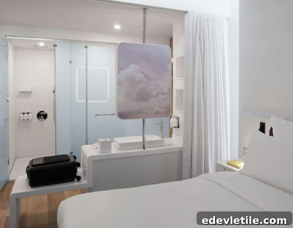 Modern minimalist hotel room at YOTEL Istanbul Airport, featuring a compact white design, open-plan bathroom, and cloud-themed divider.