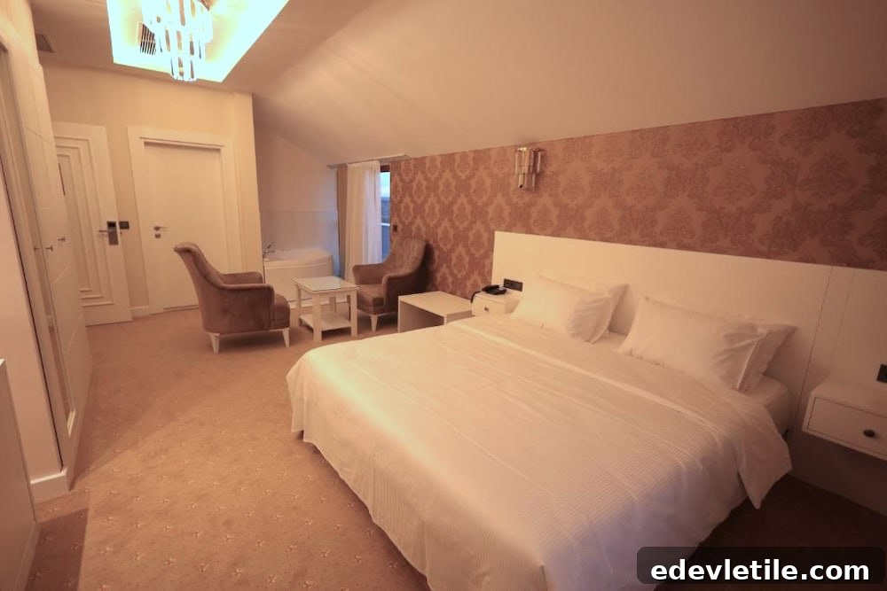 Warm-toned hotel room with sloped ceilings, a large bed, plush chairs, and a chandelier, offering a cozy stay near IST.