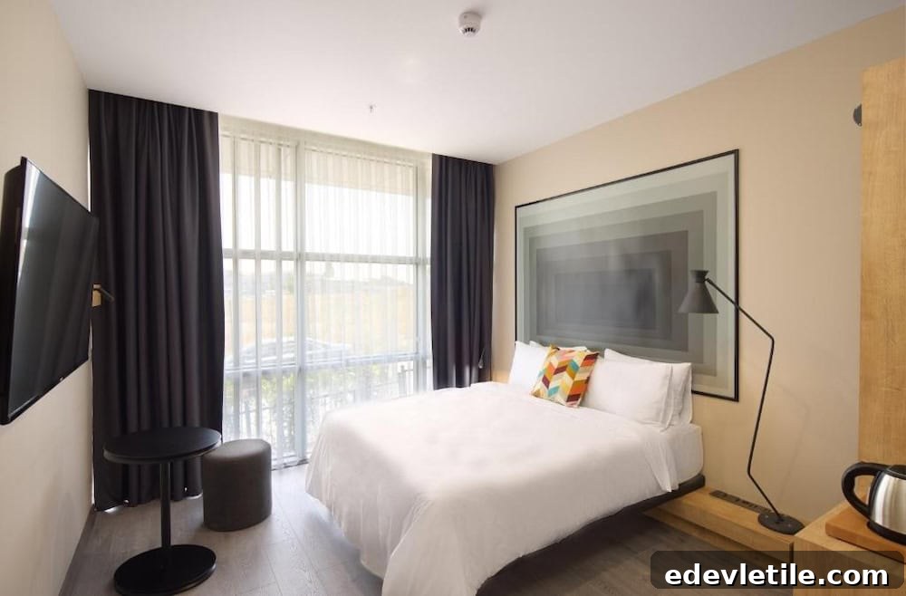 Simple and stylish hotel room with a queen bed, geometric artwork, and floor-to-ceiling windows in a hotel near IST airport