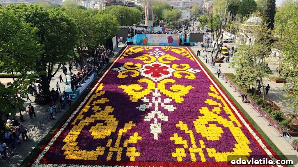 A massive tulip carpet arranged in an ornate, traditional Turkish pattern on Sultanahmet Square, viewed from above and surrounded by spectators.