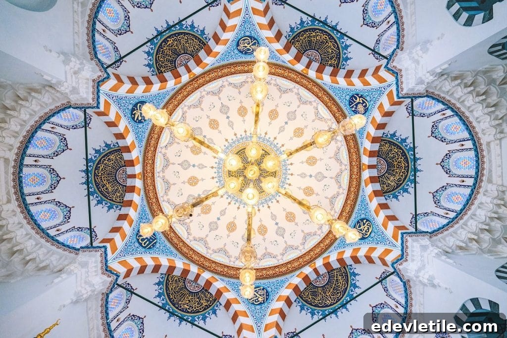 Intricately decorated dome ceiling of a mosque, featuring vibrant blue, gold, and white geometric patterns with Arabic calligraphy.