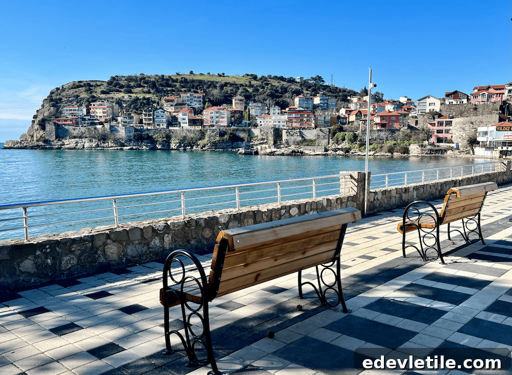 Sunny view of the Amasra seafront promenade with empty benches, overlooking the calm Black Sea and a hill dotted with homes.