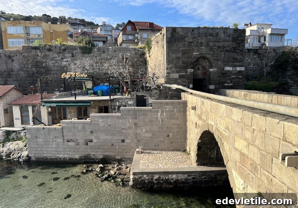 Historic Kemere Bridge leading to a medieval stone gate in Amasra, with nearby buildings and a seaside café.