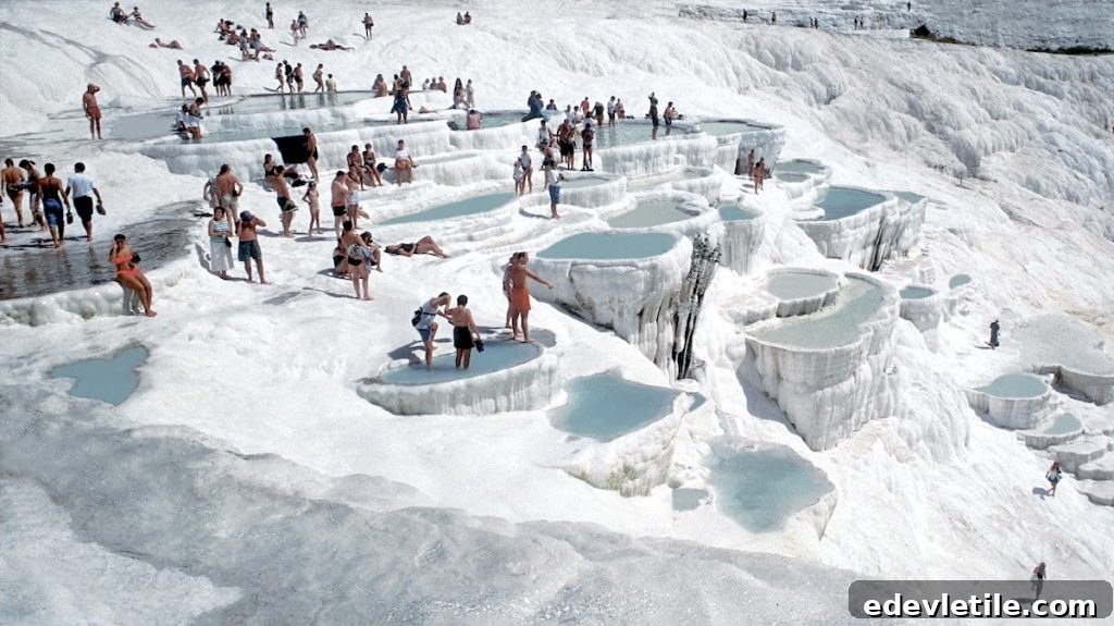 Tourists bathing in the shallow, terraced thermal pools of Pamukkale, surrounded by white calcium-rich formations.