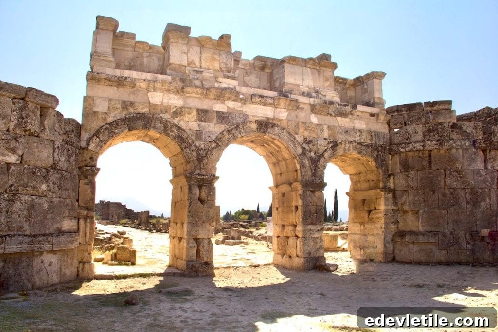 The triple-arched Roman gate at Hierapolis, the ancient city located above Pamukkale, built of weathered stone and bathed in golden sunlight.