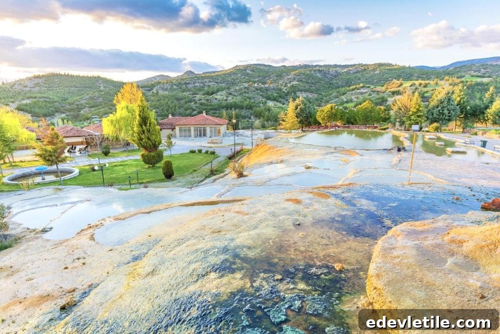 Relaxing thermal pools at a village near Pamukkale, with small buildings, landscaped gardens, and rolling green hills in the background.