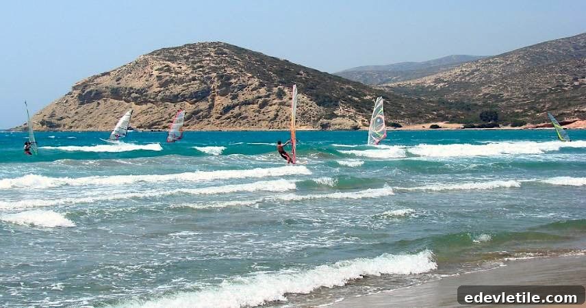 Windsurfers riding turquoise waves off the coast of Bitez with a backdrop of arid hills, showcasing the area's popularity for water sports and active beachgoers.
