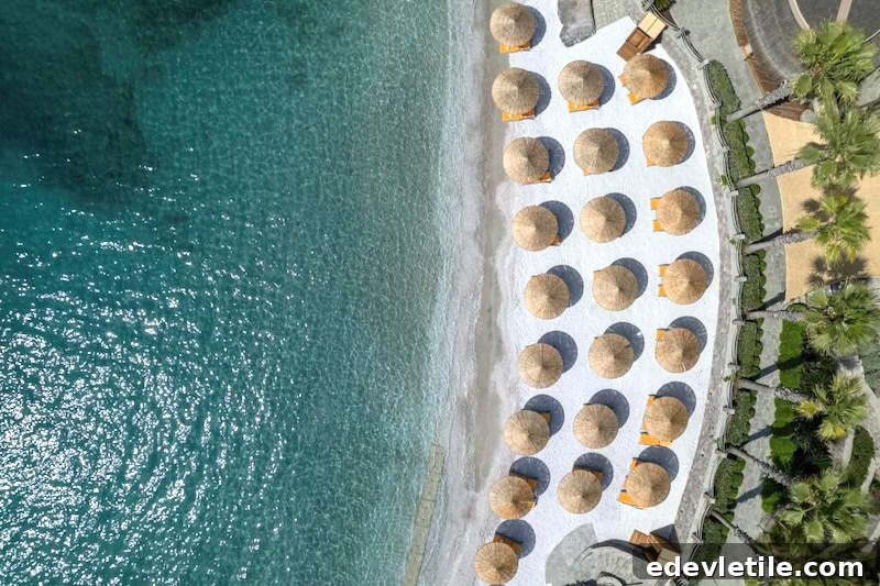Aerial view of a luxury beach in Bitez lined with thatched umbrellas and sun loungers on white sand, with calm turquoise water lapping the shore.