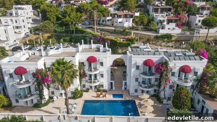 Aerial view of a charming white hotel in Akyarlar with pink bougainvillea climbing the balconies, a central pool, and surrounding greenery.