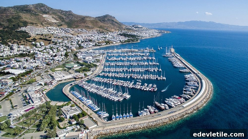 Expansive aerial view of Turgutreis Marina filled with rows of docked yachts, set against a backdrop of whitewashed buildings and rugged coastline.