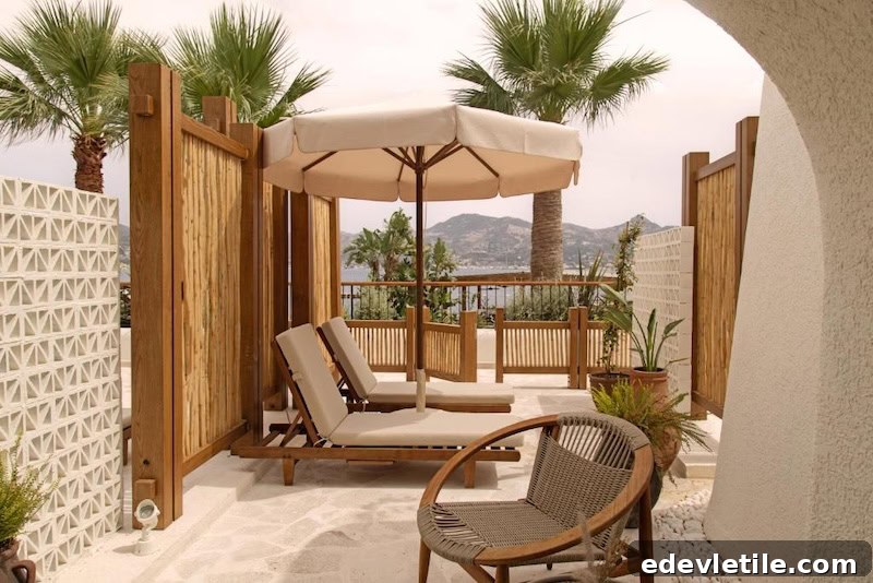 Serene private terrace with cushioned lounge chairs and umbrella, surrounded by palm trees and wood accents, overlooking the sea and hills of Göltürkbükü.