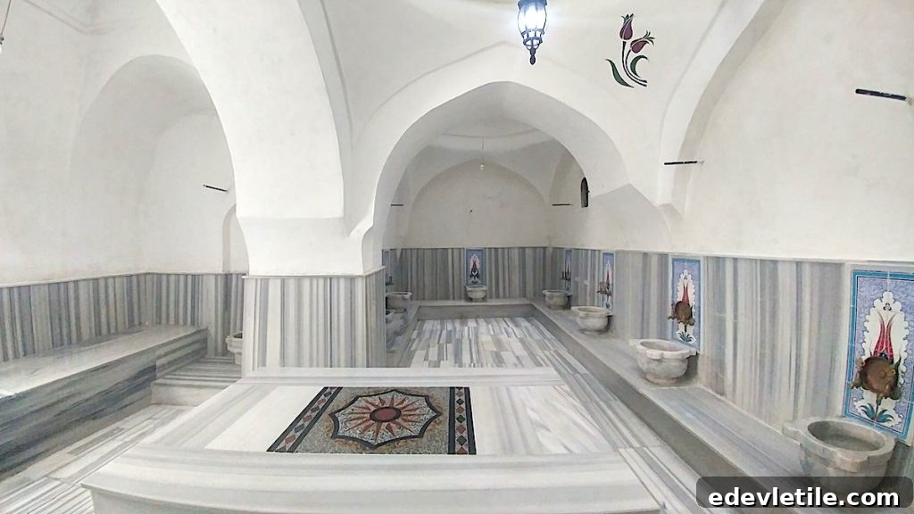 Bright white bath room at Vezneciler Hamam with tulip-patterned wall tiles, vaulted arches, and multiple marble basins surrounding the platform.