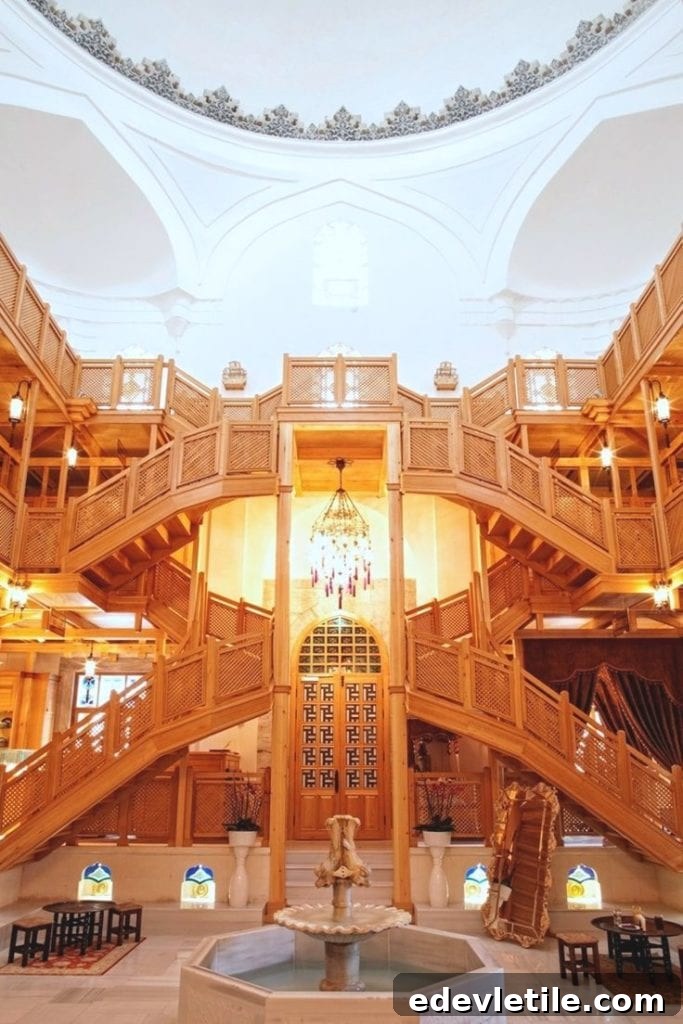 Interior of Hurrem Sultan Hammam showcasing elaborate wooden staircases, chandeliers, and a central fountain beneath a grand white dome.