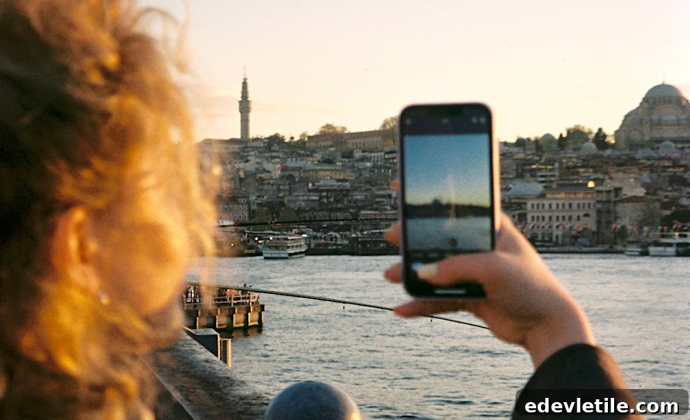 A woman taking a smartphone photo of Istanbul’s skyline and mosques at sunset from the waterfront.