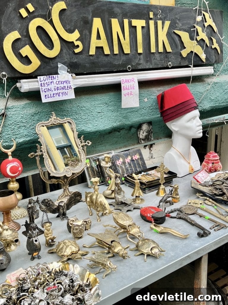 Outdoor table at Göç Antik in Balat covered with brass figurines, old keys, trinkets, and a mannequin head wearing a red fez hat under a bold black and gold sign.