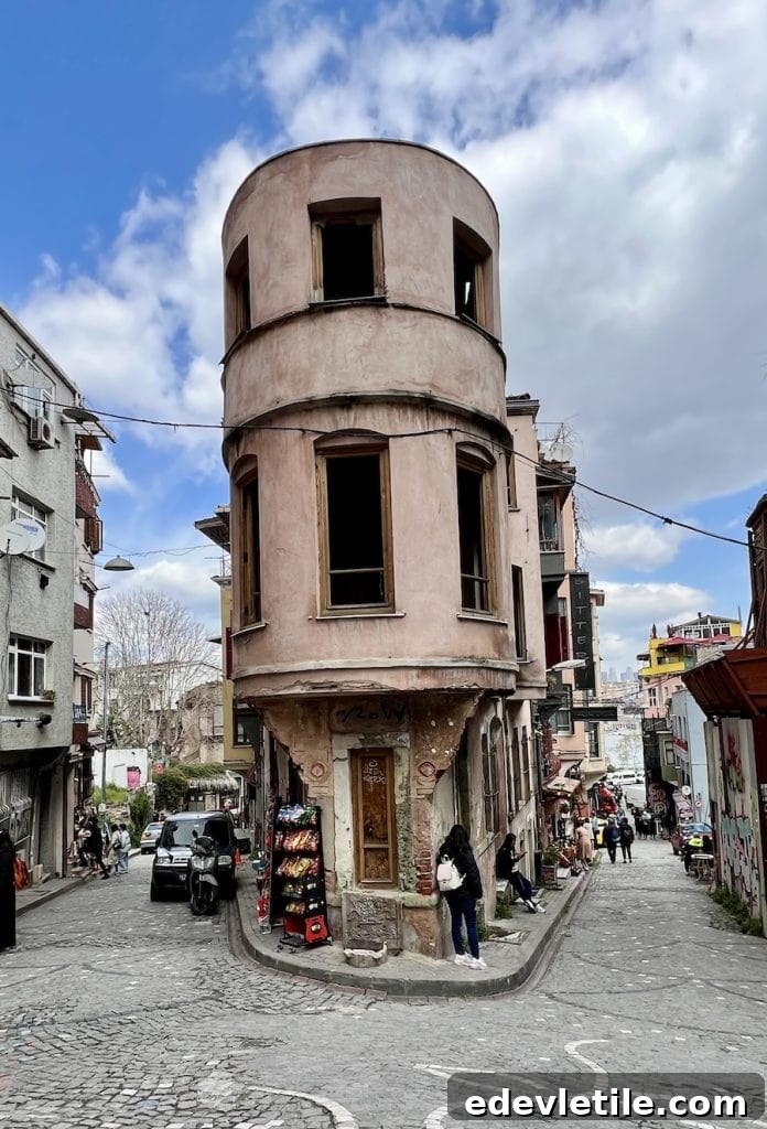 Narrow, curved historic building sitting at a fork in the cobblestone streets of Balat, with weathered pink exterior and snack stand at the corner.