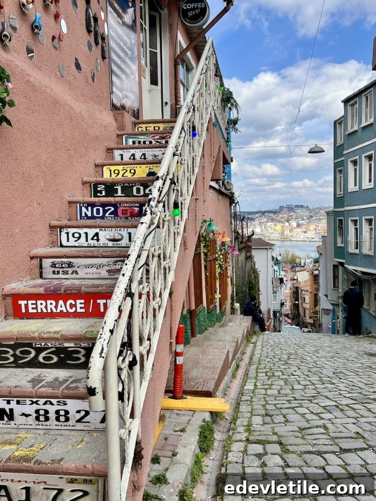 Quirky staircase decorated with vintage license plates leading to a cafe terrace in Balat, overlooking a hilly street and golden Horn skyline in the distance.