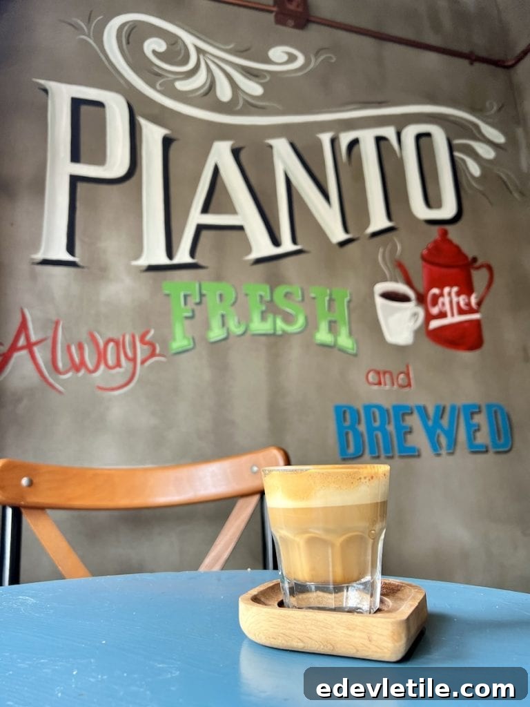 Close-up of a fresh coffee served in a small glass on a blue table at Pianto Cafe in Balat, with the mural reading “Always Fresh and Brewed” in the background.