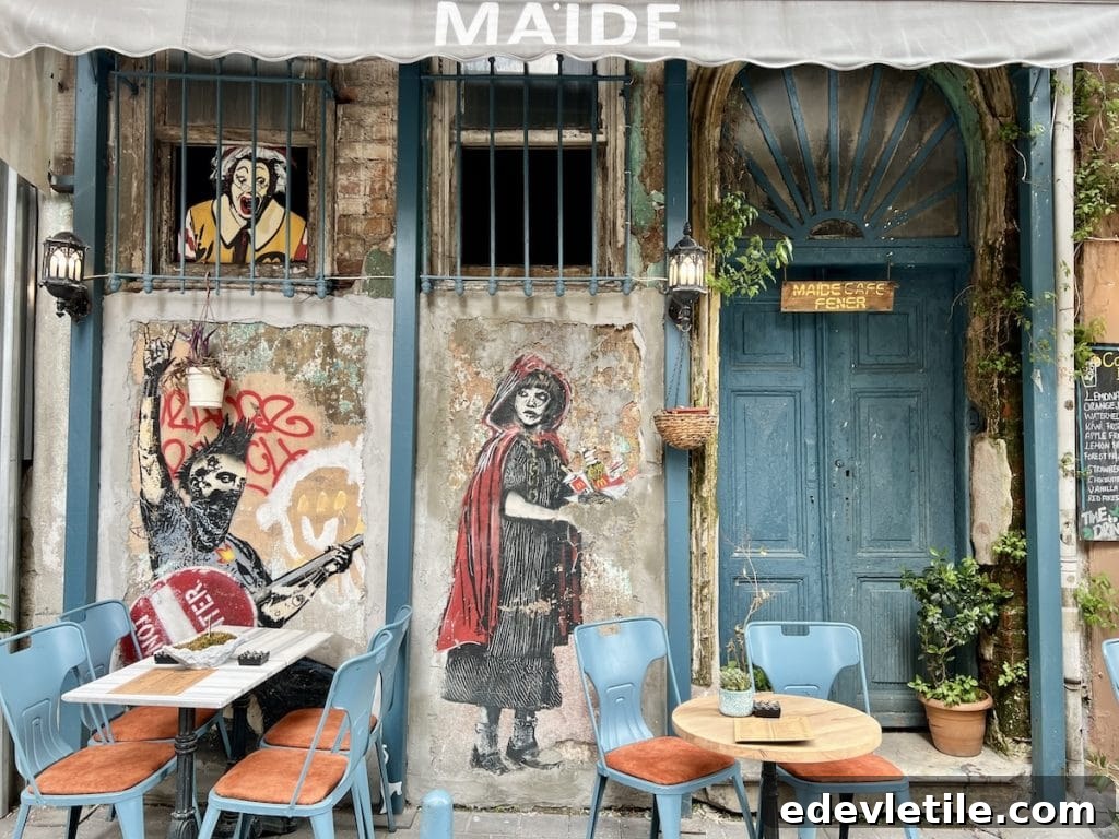 Outdoor tables and chairs at Maide Cafe in Balat, with artistic murals of characters painted on the weathered stone walls behind blue doors and windows.