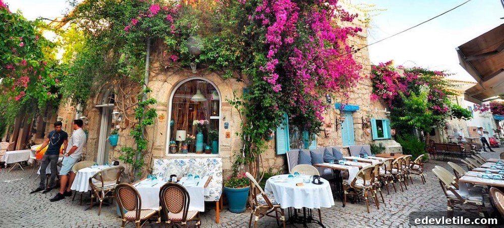 Colorful outdoor cafe in Alaçatı with cobblestone streets, blooming bougainvillea, and stone buildings with turquoise shutters.