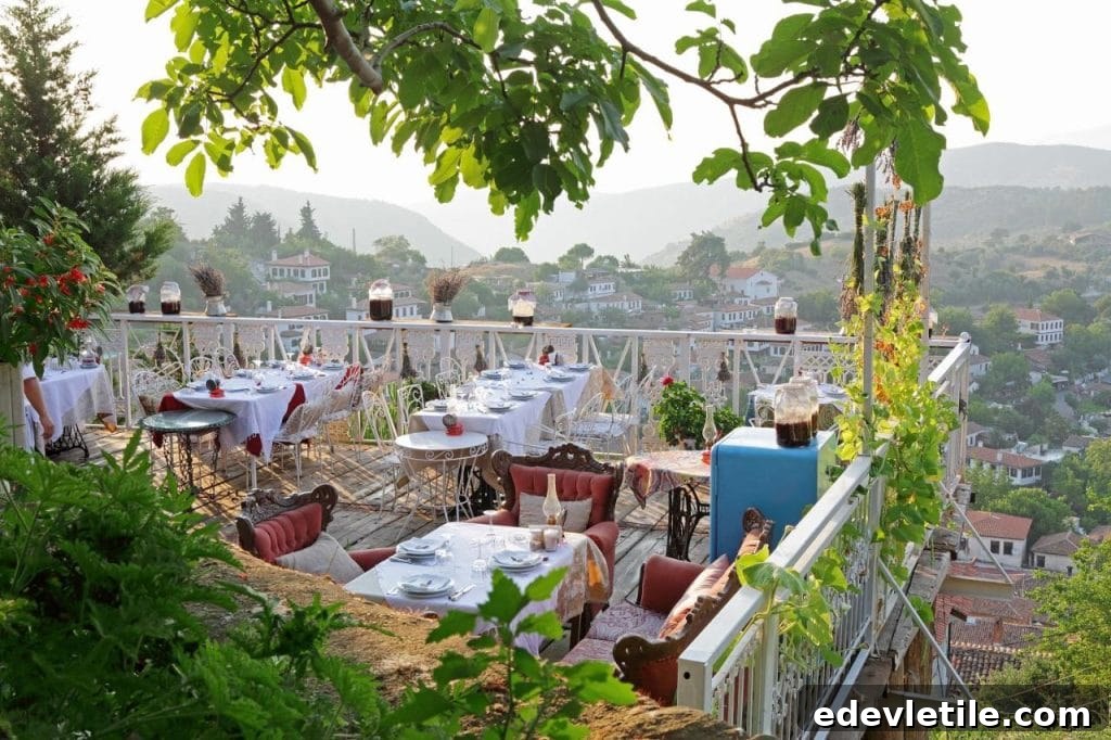 Charming hilltop restaurant terrace decorated with colorful table settings, overlooking the red rooftops and forested hills of Şirince.