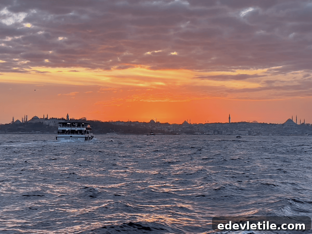 Passenger boat sailing on the Bosphorus at sunset, with vivid orange skies and Istanbul’s skyline silhouetted in the distance, including iconic mosques.
