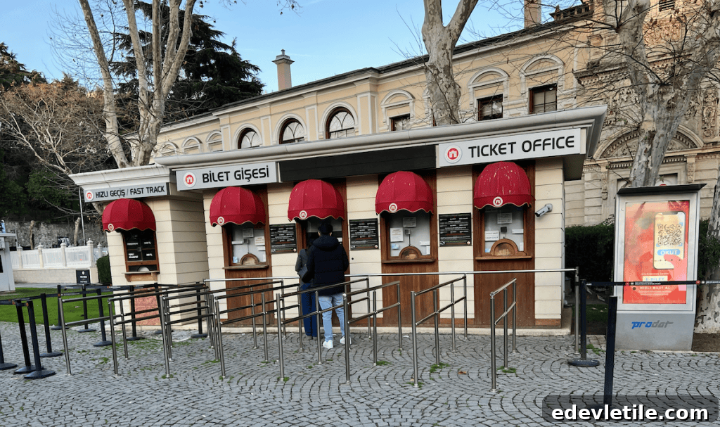 Outdoor ticket booth at Dolmabahçe Palace with red awnings, signage in Turkish and English, and visitors queuing on a cobblestone path.