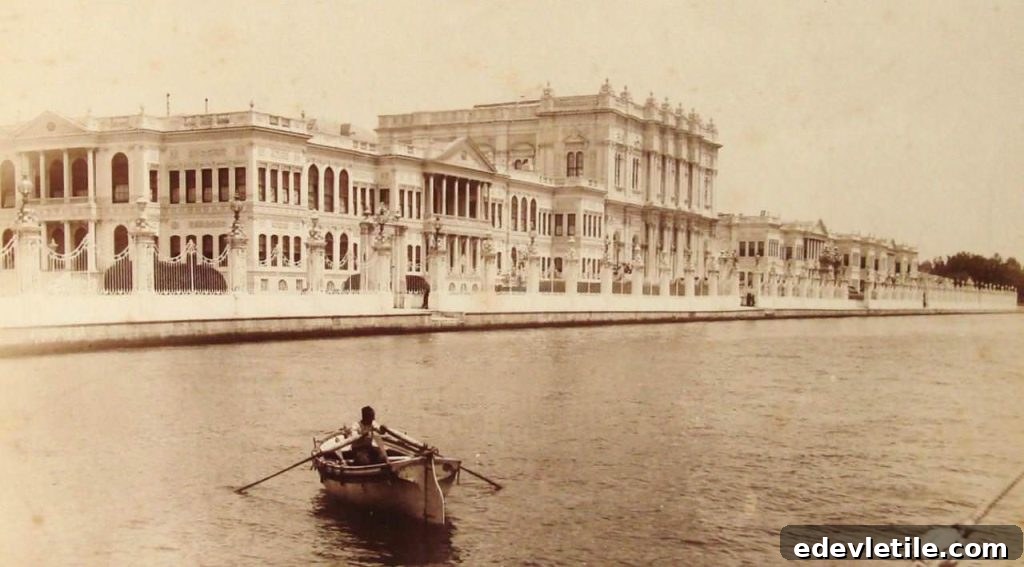 Sepia-toned historical image showing the Dolmabahce palace’s waterfront façade with a man rowing a small boat in the foreground.