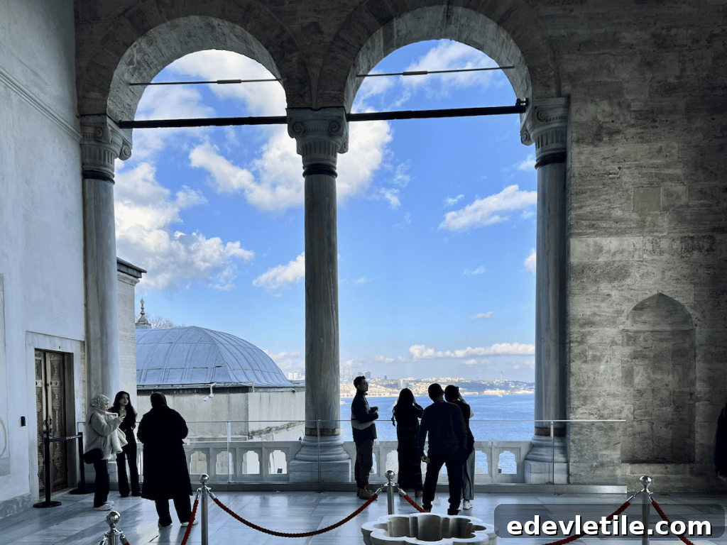Visitors admire the Bosphorus from a marble terrace in the fourth courtyard of Topkapi Palace, framed by grand archways and stone columns.