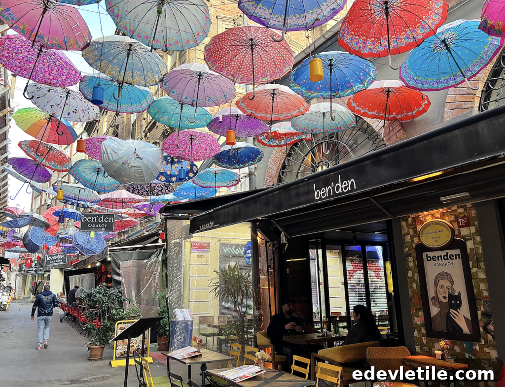 Colorful umbrellas hang overhead along a narrow pedestrian street in Karaköy, Istanbul, lined with cafes and restaurants