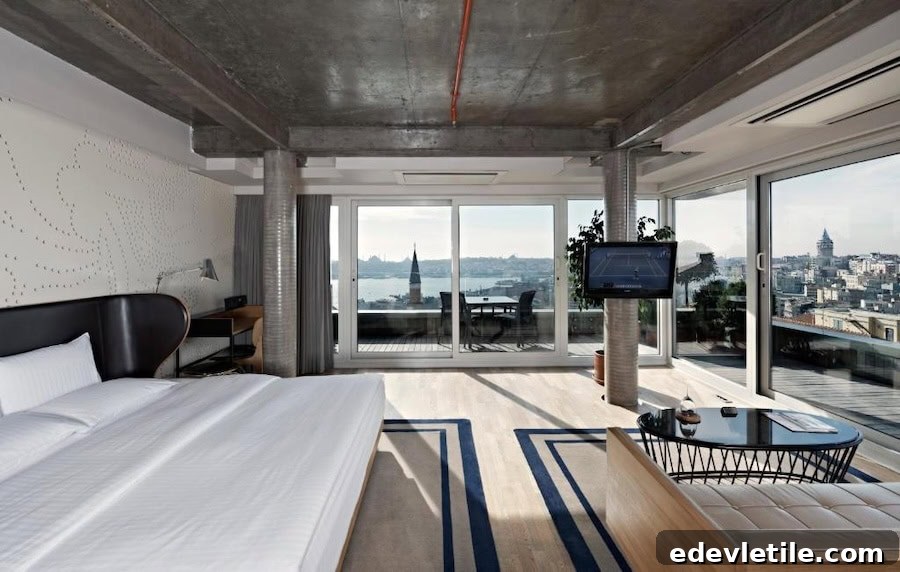 Spacious modern suite at Witt Istanbul Suites with industrial ceilings, a large bed, and floor-to-ceiling windows showcasing the Bosphorus and Galata Tower.