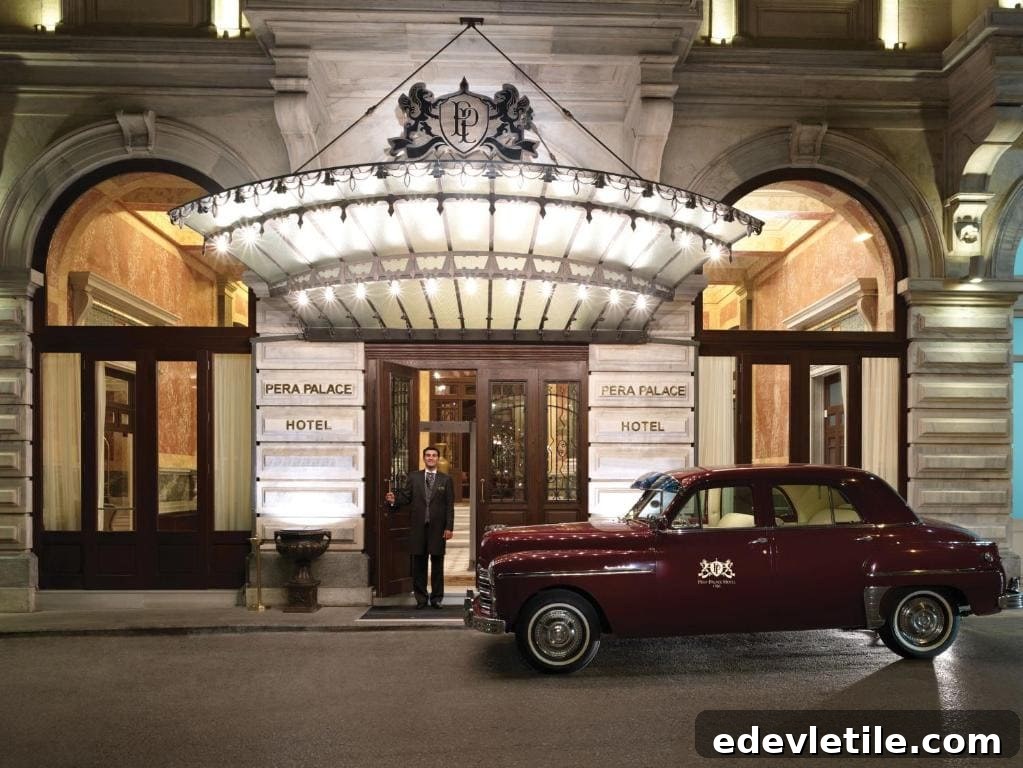 Elegant exterior of Pera Palace Hotel at night, featuring a grand, illuminated canopy and a vintage burgundy car parked at the entrance with a doorman welcoming guests.