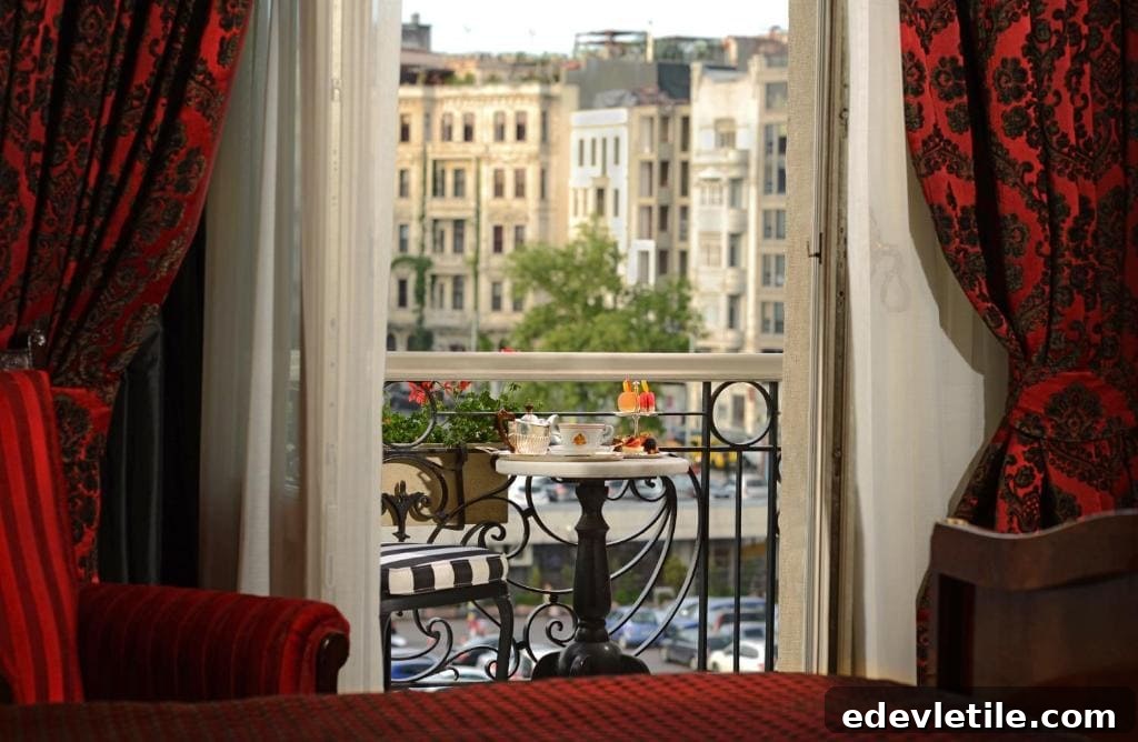 A charming balcony at Pera Palace Hotel overlooking historic Beyoğlu buildings, with a small table set for afternoon tea and pastries framed by deep red curtains.
