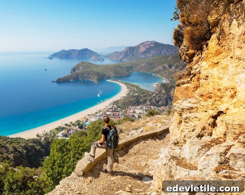 A hiker gazes over the turquoise waters and curved white beach of Ölüdeniz Lagoon from a rocky trail along the Lycian Way.