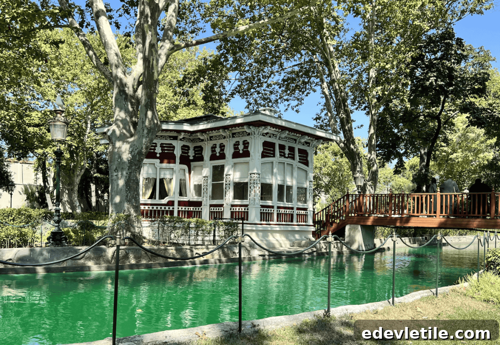 Picturesque Island Pavilion (Ada Köşkü) at Yıldız Palace, with intricate white woodwork and a red bridge over the green canal, shaded by tall trees.