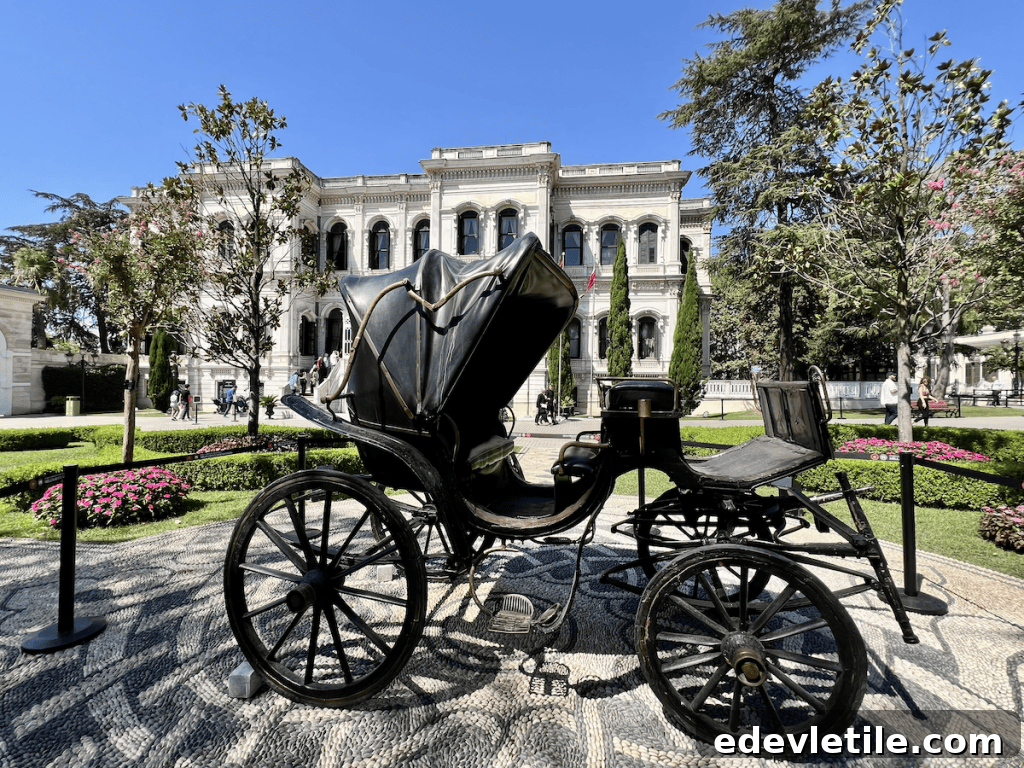 Vintage black horse-drawn carriage on display in the garden of Yıldız Palace, surrounded by manicured flower beds and tall trees.