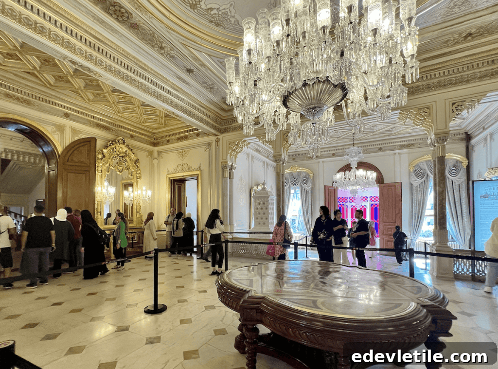 Lavish interior of Yıldız Palace’s main hall with visitors touring under ornate ceilings, a massive crystal chandelier, and marble flooring.